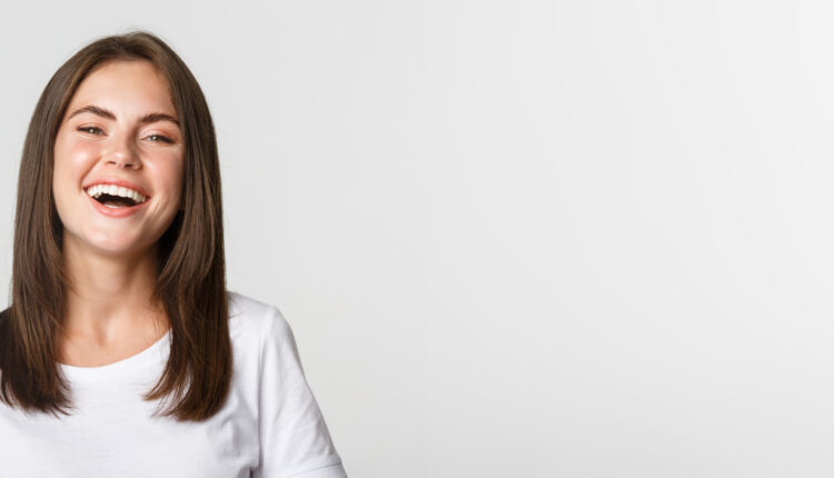 Close-up of happy brunette girl in white t-shirt laughing and smiling carefree at camera.